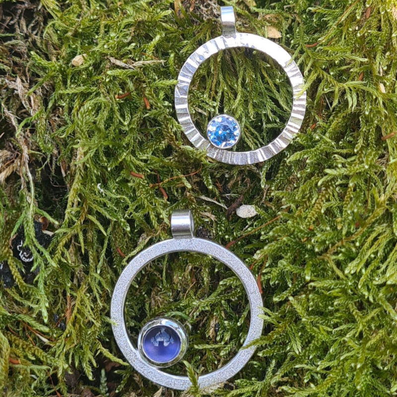 Kreisförmige silberne Anhänger mit blauen Steinen auf Moos
